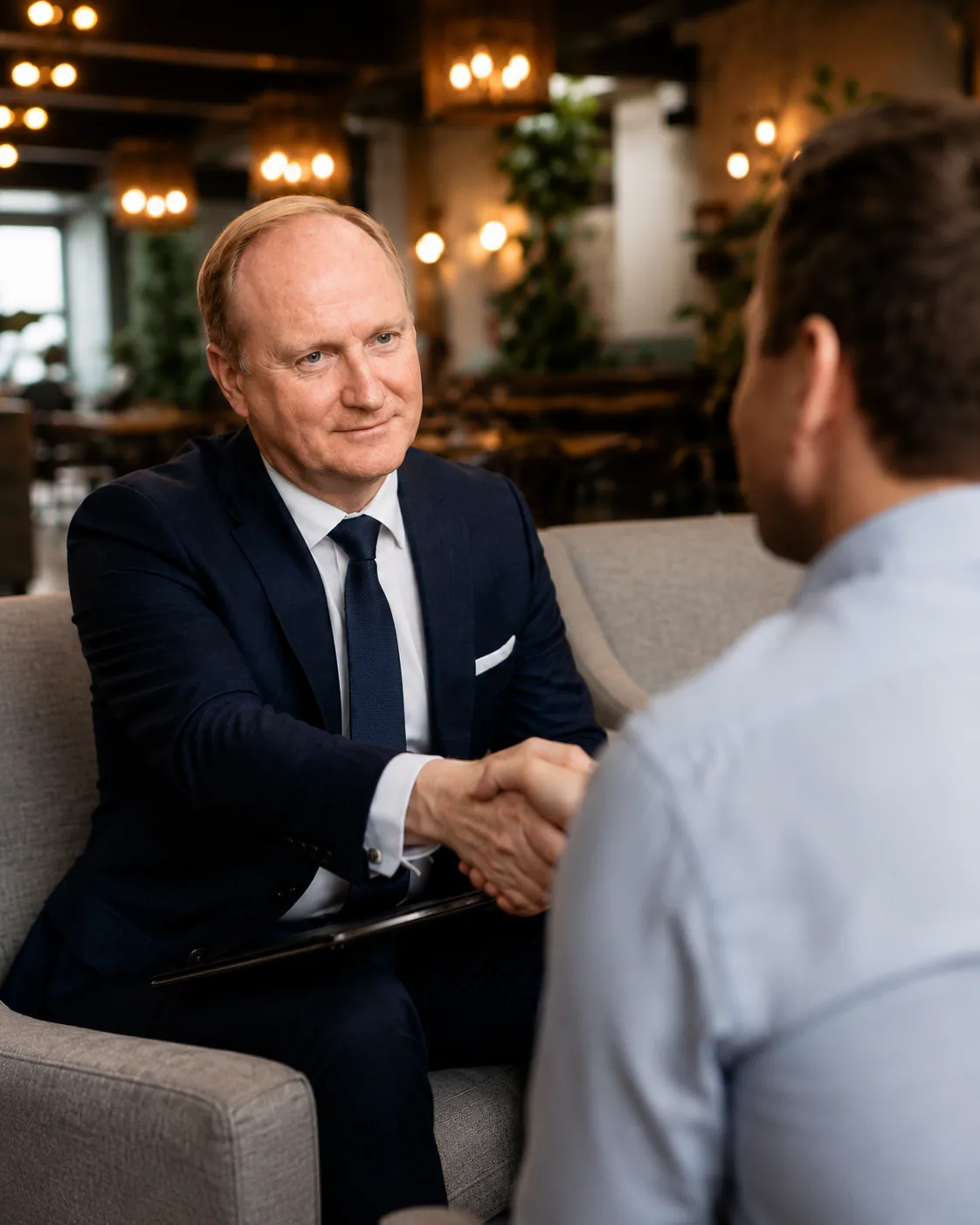 Capital Unique — a handshake between two executives across a coffee table in a warm restaurant lounge.